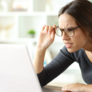 Woman wearing eyeglasses having vision problems forcing sight watching online content on laptop at home