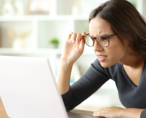 Woman wearing eyeglasses having vision problems forcing sight watching online content on laptop at home