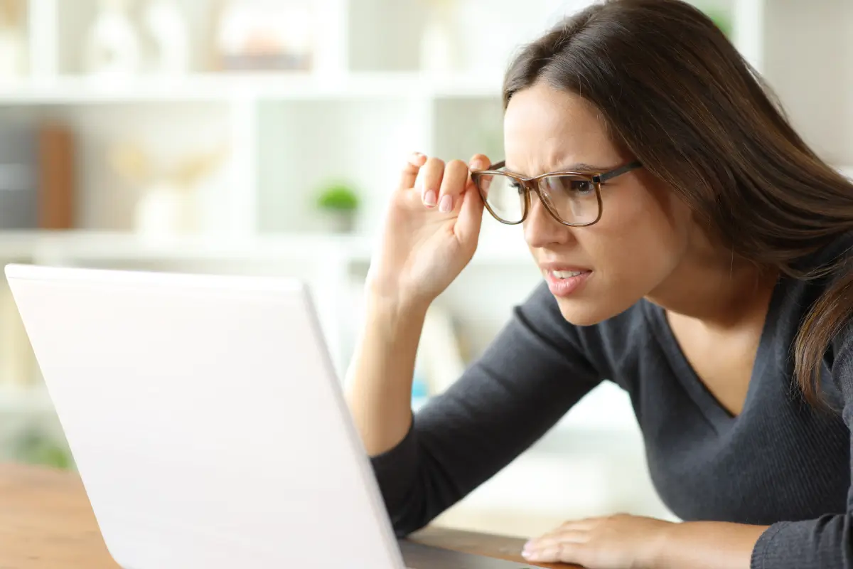 Woman wearing eyeglasses having vision problems forcing sight watching online content on laptop at home